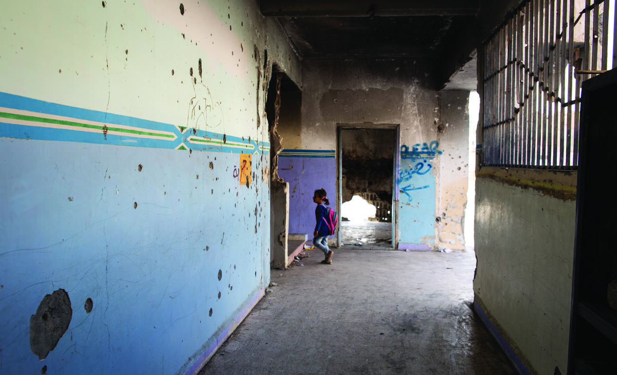 Jente går inn i et klasserom. Skolen er ødelagt etter bombeangrep. 