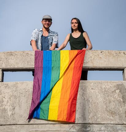 To mennesker henger regnbueflagg over bro
