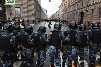 Russiske sikkerhetsstyrker står oppstilt foran demonstranter og mennesker i en gate. 