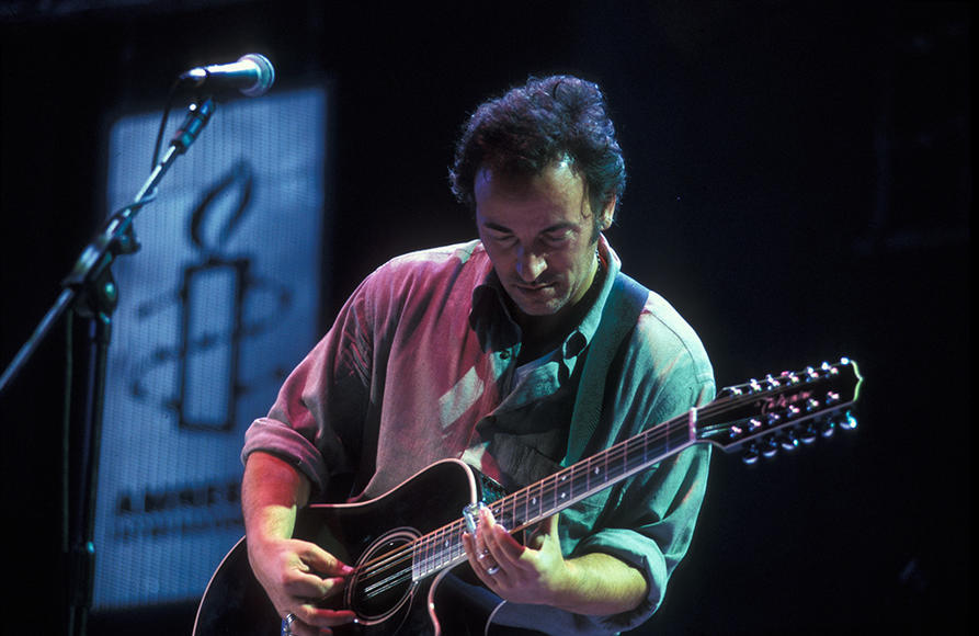 Bruce Springsteen spiller gitar. Plakat av Amnesty-logoen i bakgrunnen. 