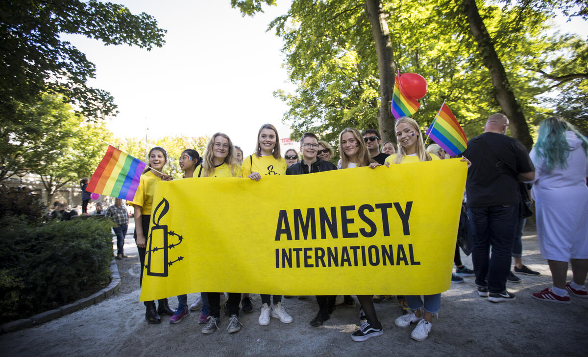 Ungdommer på Pride står bak et Amnesty-banner og smiler til kamera. 