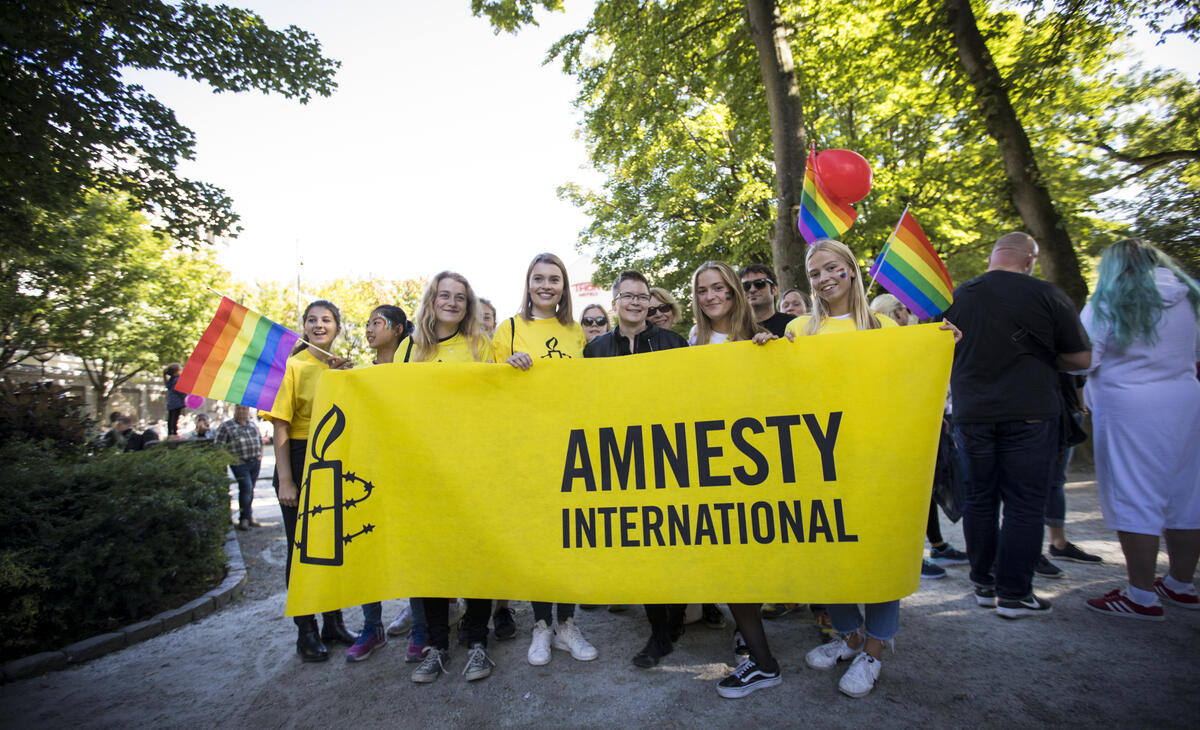 Ungdommer på Pride står bak et Amnesty-banner og smiler til kamera.