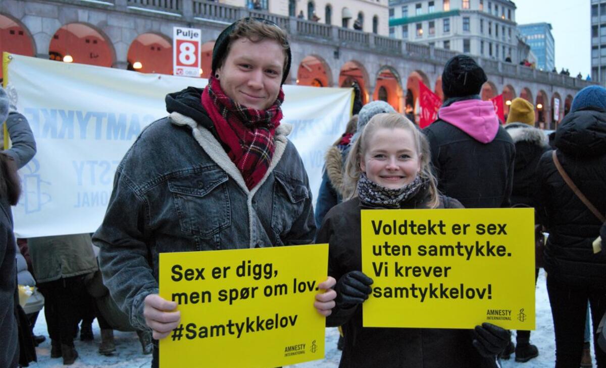 Mann og kvinne står med plakater under 8. mars-markering. Plakatene sier "Sex er digg, men spør om lov. Samtykkelov nå!"