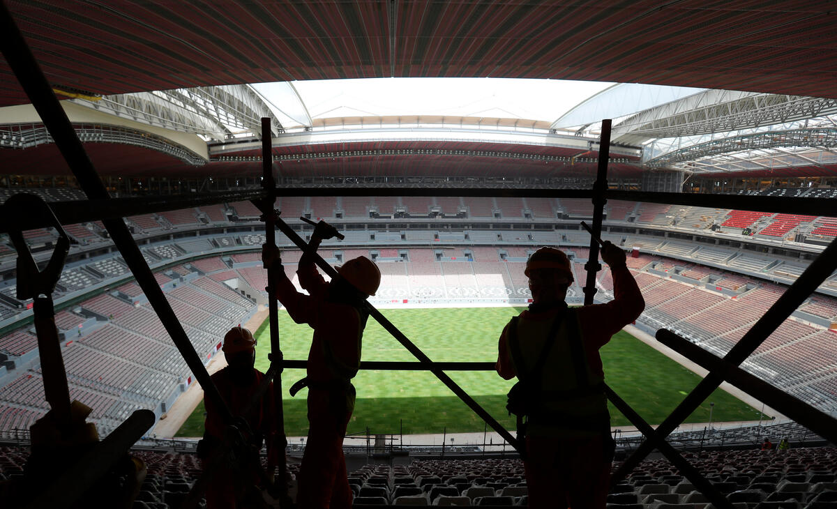 Bildet viser tre arbeidere og et fotballstadion