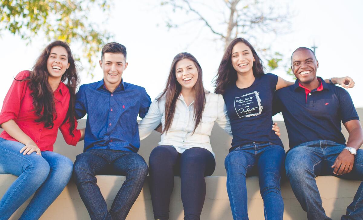 En gruppe med fem unge mennesker sitter på en benk og smiler til kamera