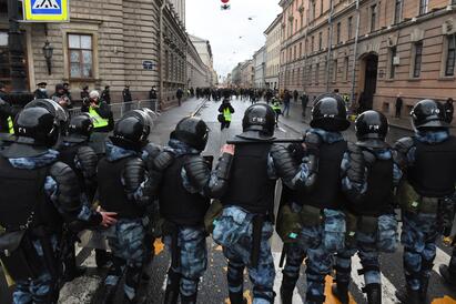 Russiske sikkerhetsstyrker står oppstilt foran mennesker og demonstranter i en gate. 