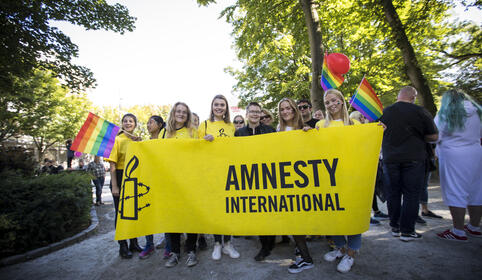 Ungdommer på Pride står bak et Amnesty-banner og smiler til kamera. 