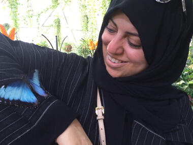 En kvinne i sorte klær viser frem en blå sommerfugl som sitter på armen hennes