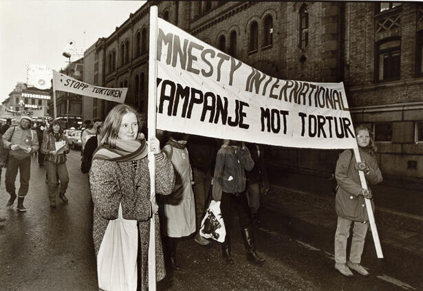 Nordmenn marsjerer mot tortur.  Kvinne holder banner med teksten "Kampanje mot tortur".