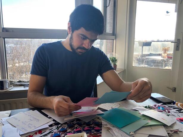 En mann sitter ved et bord og leser brev i forskjellige farger