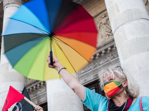 Kvinne demonstrerer i Polen. Hun har munnbind og en paraply i regnbuefarger. 